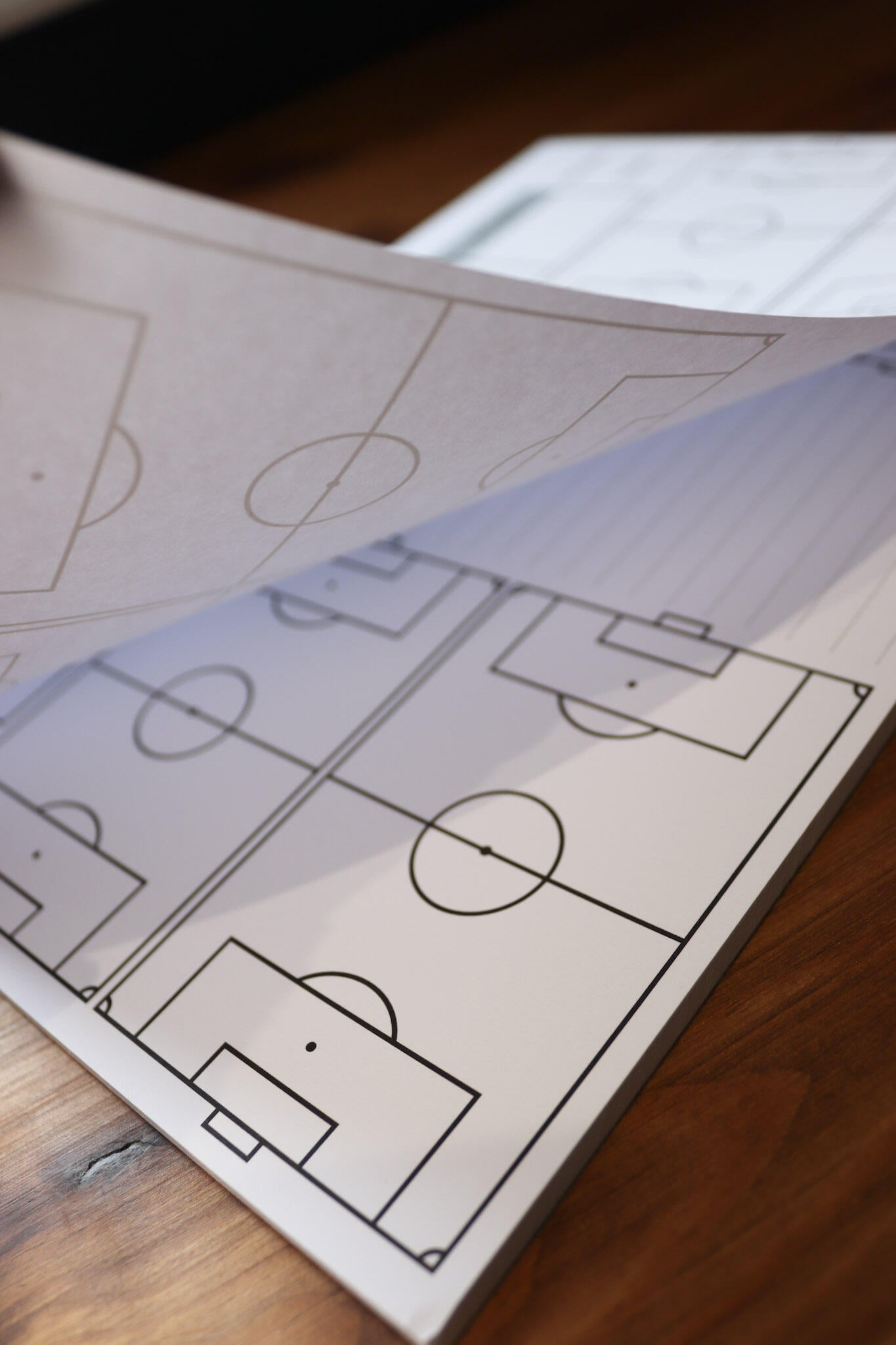 Fanned pages of an Allenatori Club coaching notebook on a wooden surface, each displaying blank football pitch diagrams for tactical planning.