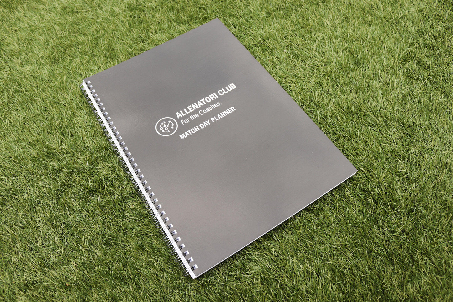 Allenatori Club Match Day Planner spiral-bound notebook with dark grey cover on green grass.