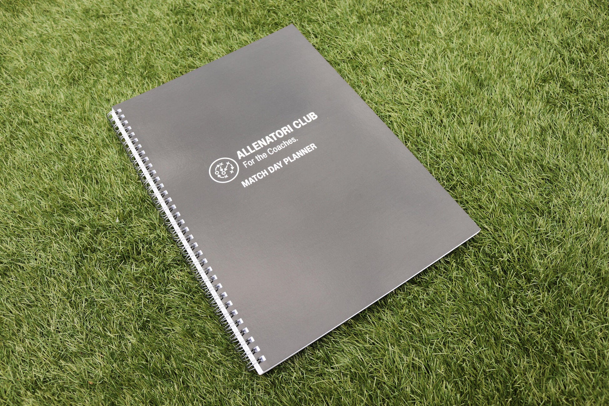 Allenatori Club Match Day Planner spiral-bound notebook with dark grey cover on green grass.